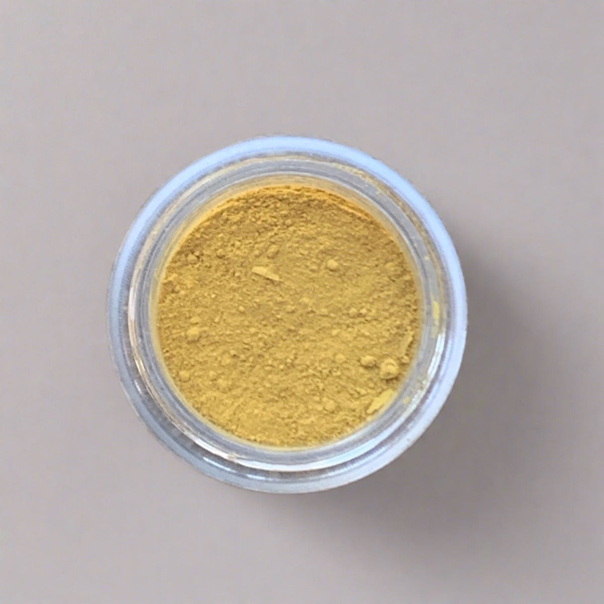 Cosmetic jar of light yellow eyeshadow loose powder, displaying its color and texture