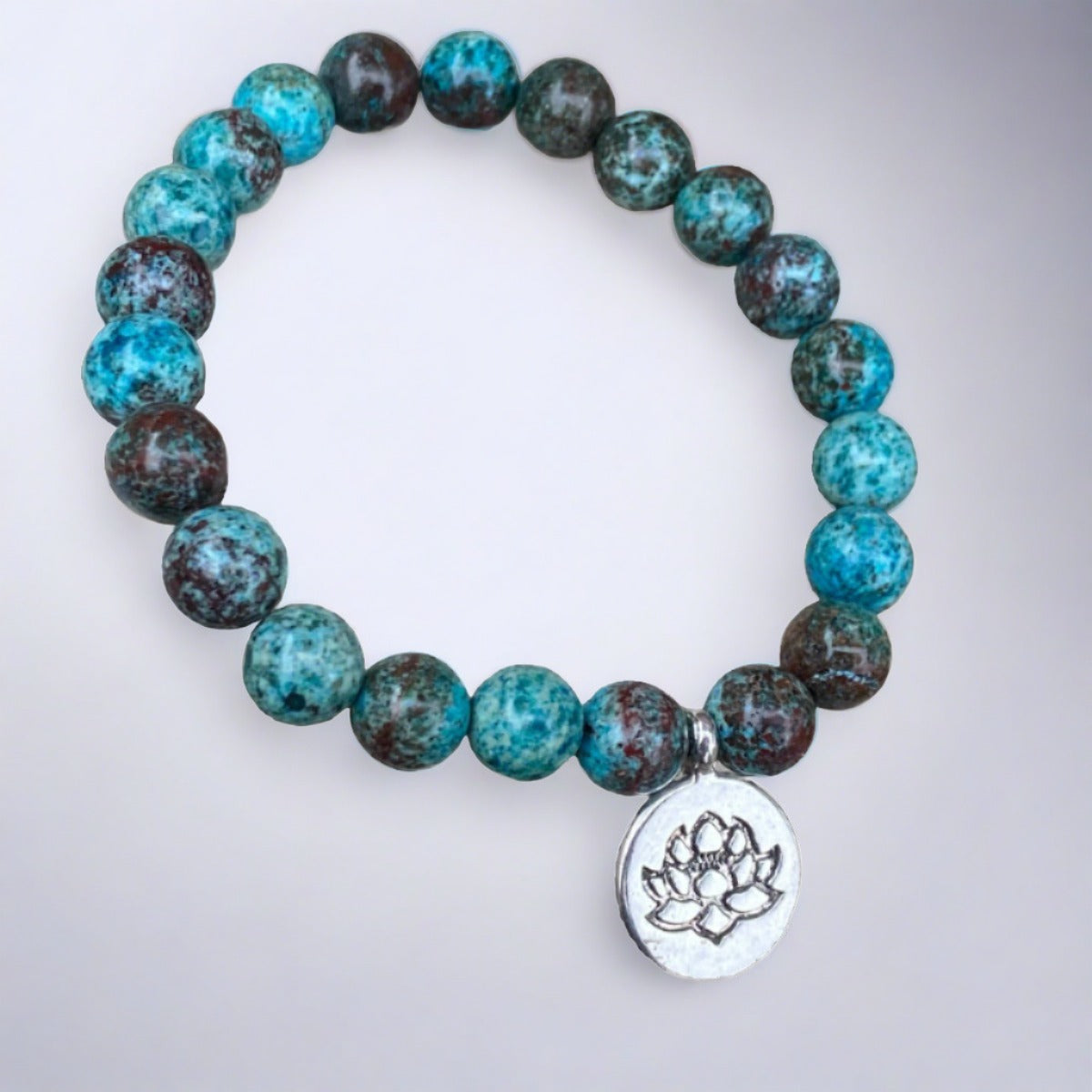Blue chrysocolla bracelet with lotus charm on rock background