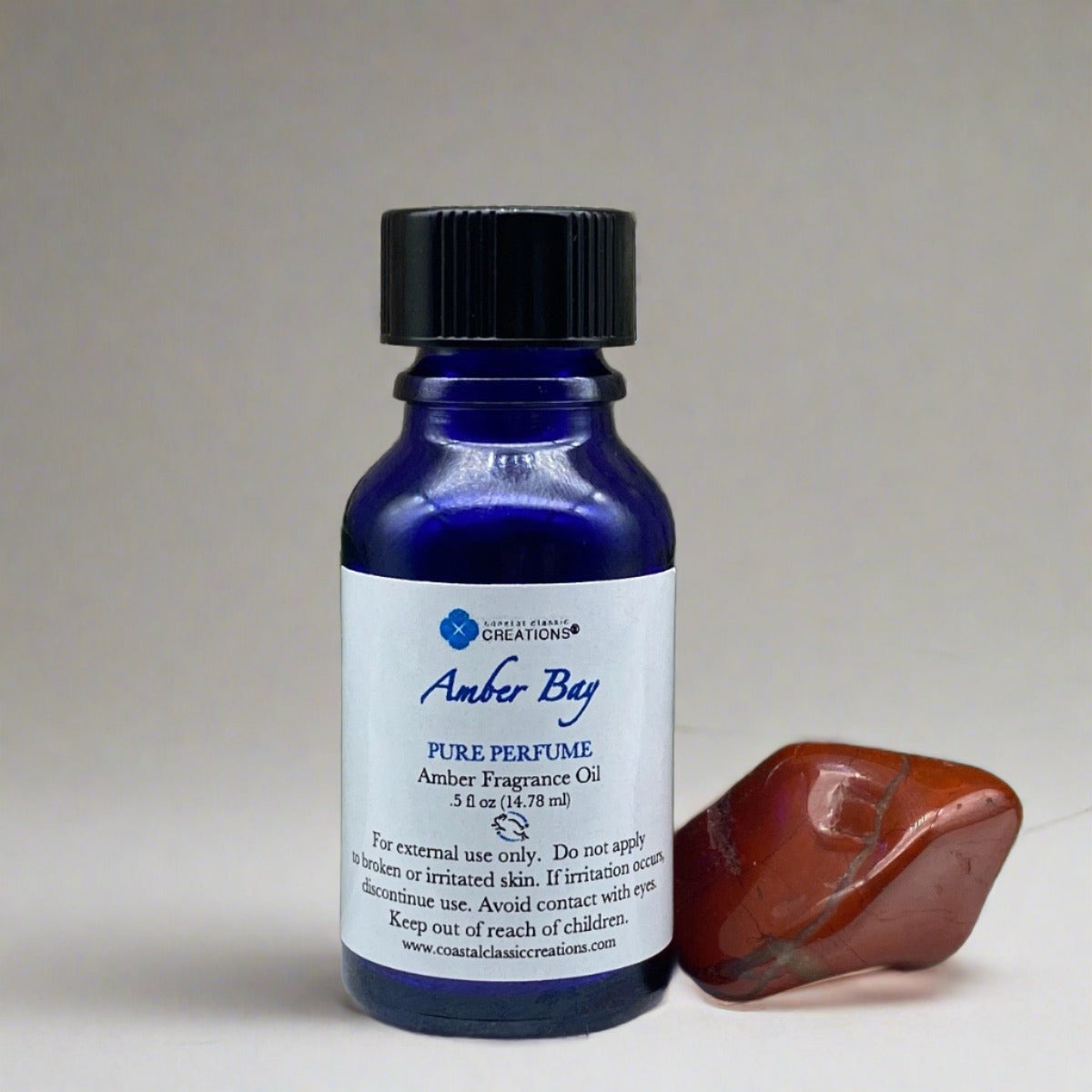 Half-ounce blue bottle of Amber Bay Amber Perfume with a black cap, labeled with the product name and ingredients, featuring a sleek, cylindrical shape