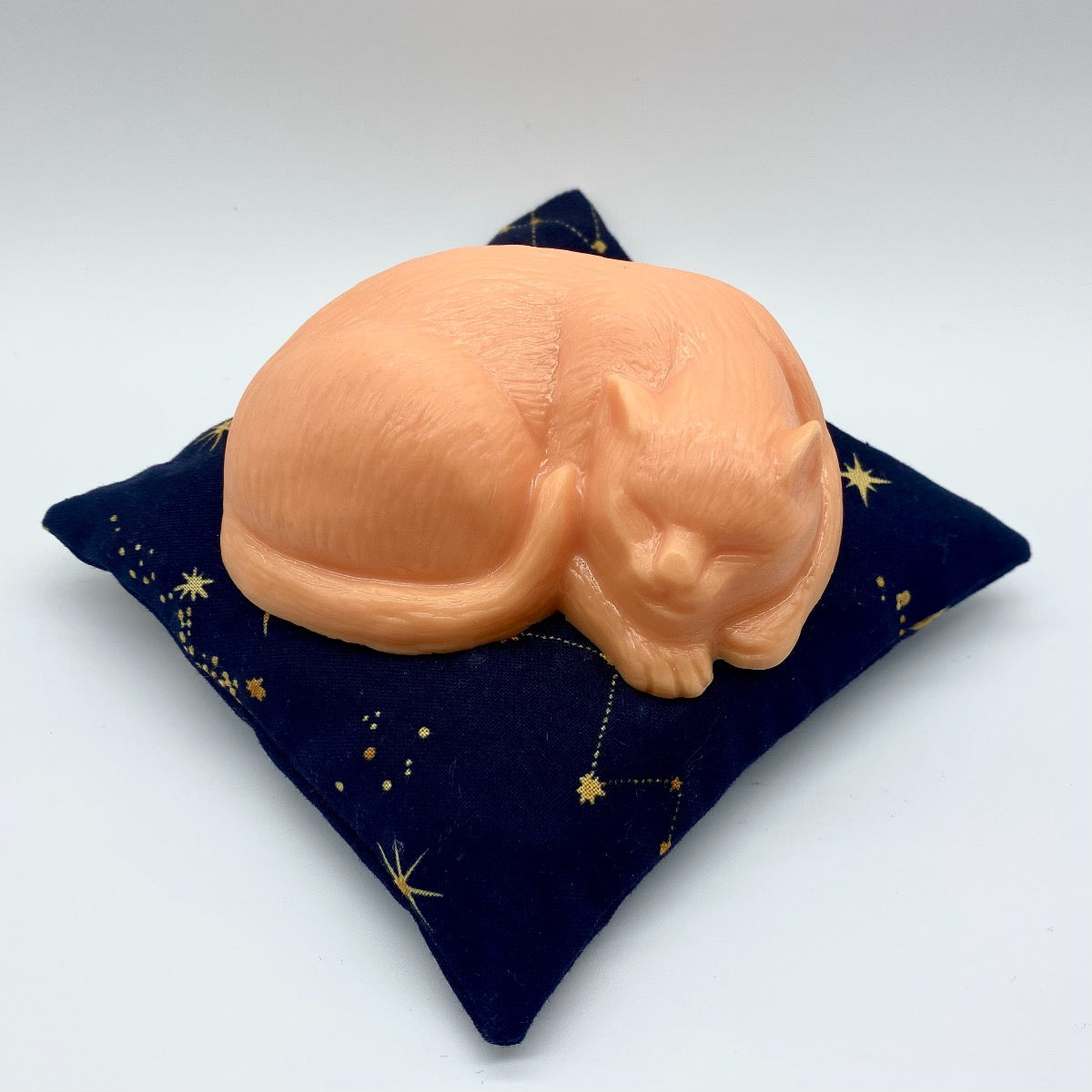 Mindfully sleeping orange cat-shaped soap, representing the essence of mindful beauty, resting on a celestial navy blue pillow with stars