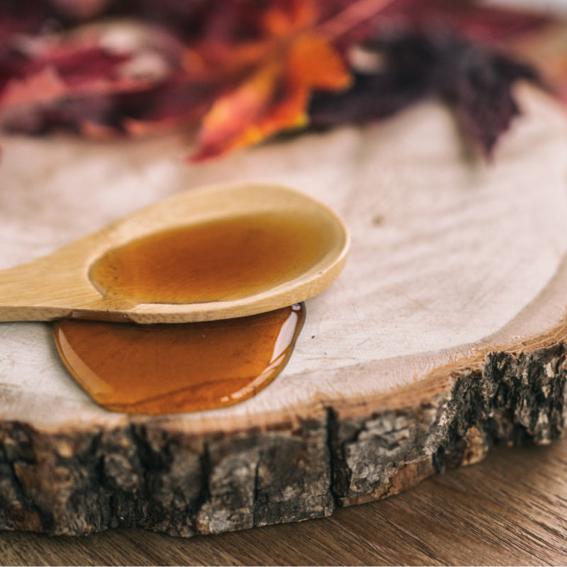 Wooden spoon filled with maple syrup on top of wooden coaster representing product fragrance