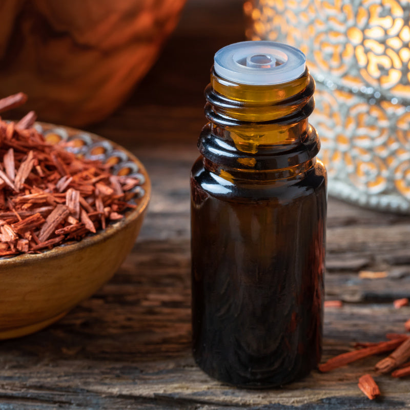 Bottle of sandalwood oil with dried sandalwood and candle in the background