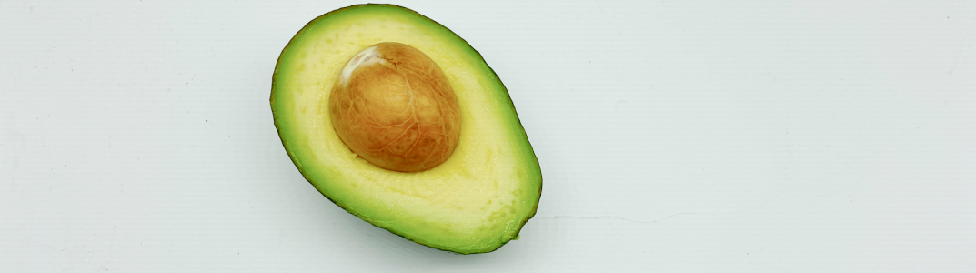 A half of a fresh avocado with the pit on a white background