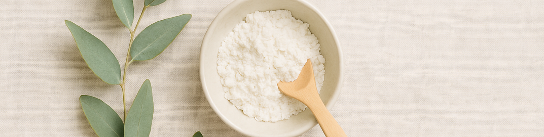 Small bowl of cornstarch with wooden spoon and eucalyptus leaves on a beige banner