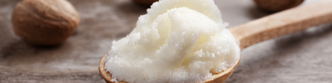 Wooden spoon with a scoop of white shea butter on a wooden surface
