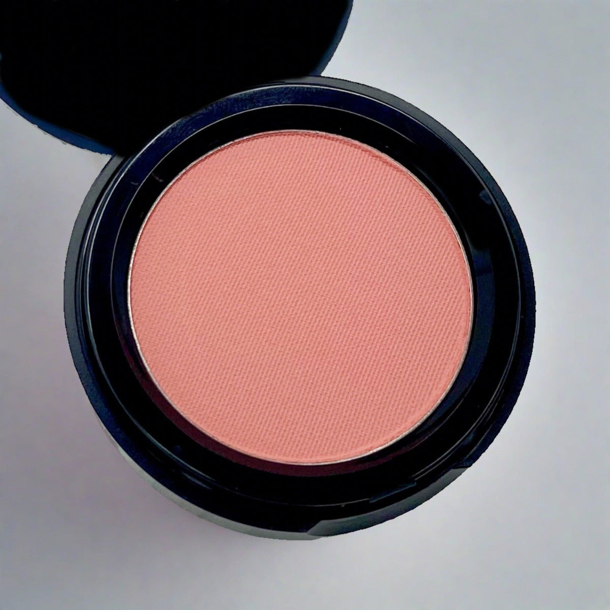  Cosmetic container of peach pink matte pressed blush displaying its color and texture