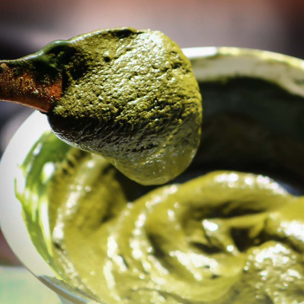 Thick green henna paste on a wooden spoon above a bowl, made from natural ingredients and free from synthetic chemicals