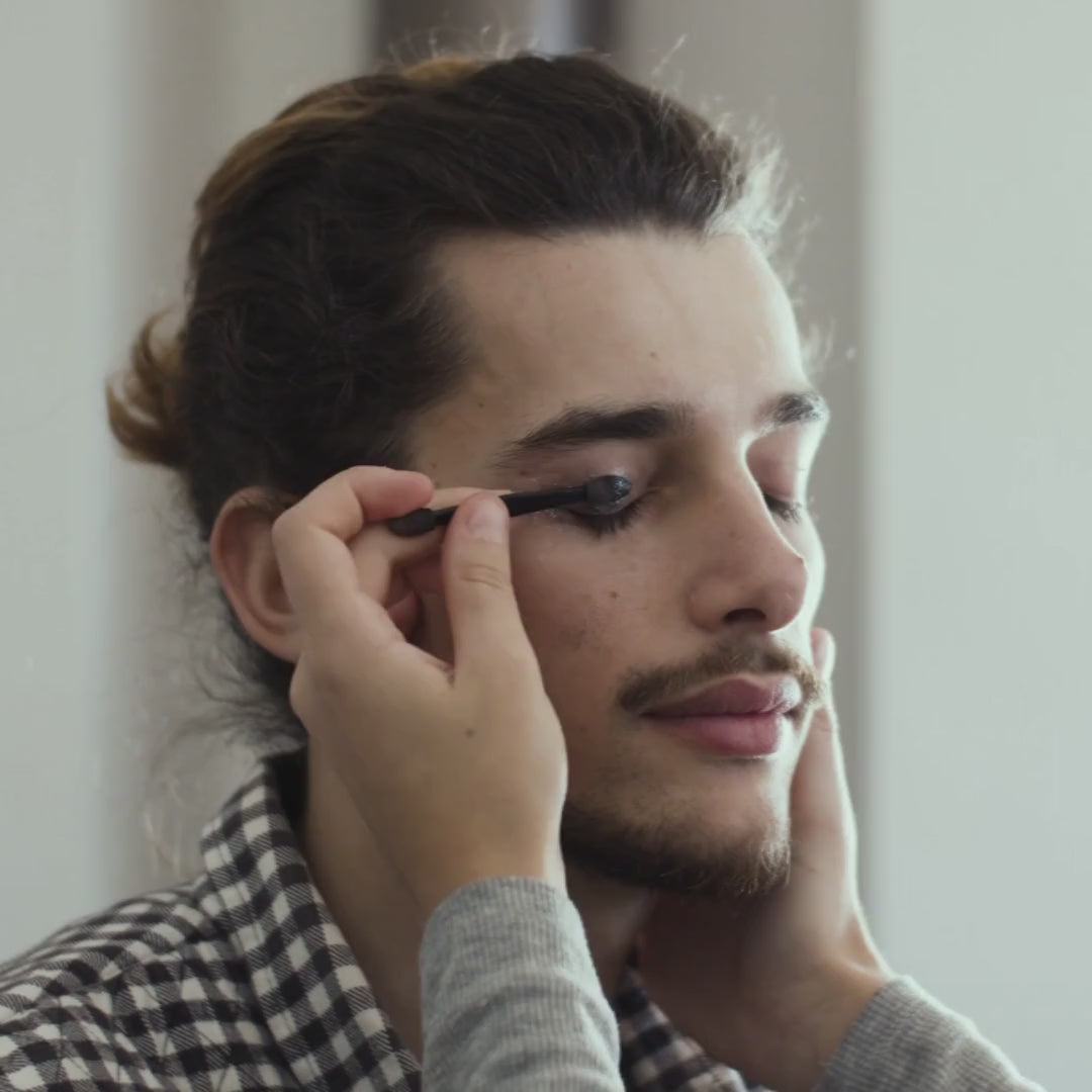 A man’s eyelid being brushed with deep sea blue matte eyeshadow, showing bold, artistic color application.