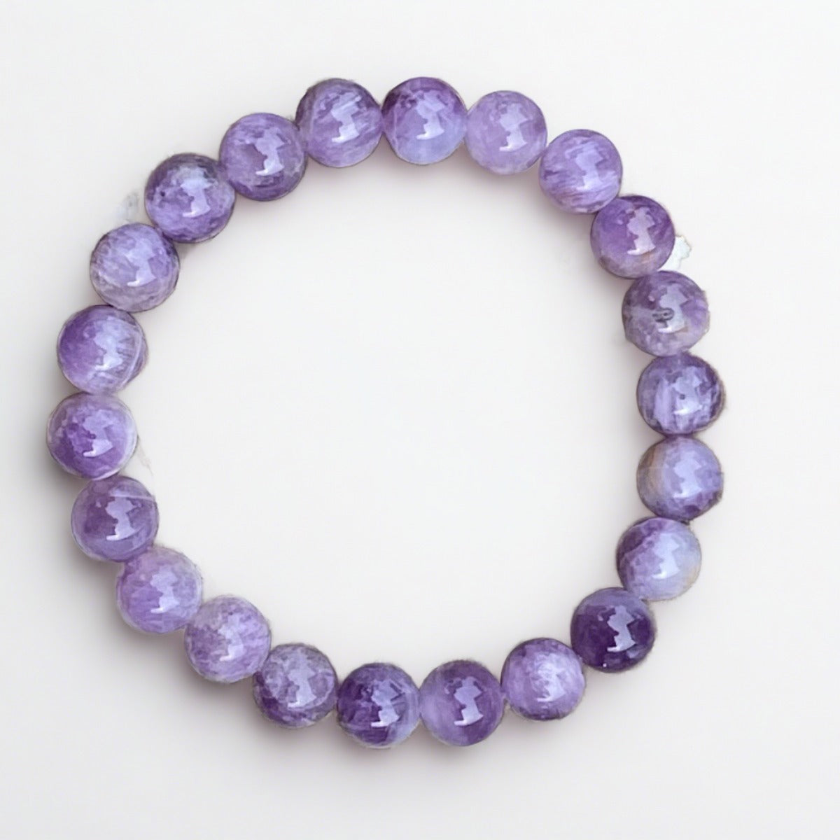 A white and brown rock featuring the Crown Chakra Dogtooth Amethyst Motivation Bracelet by Coastal Classic Creations, symbolizing mindfulness and spiritual connection