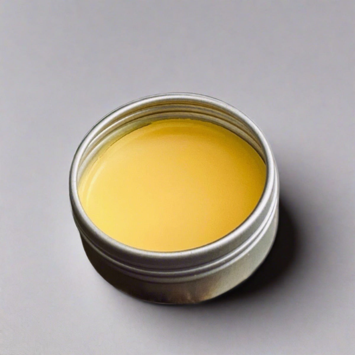 Small tin of orange butter lip balm showcasing its orange color and creamy texture