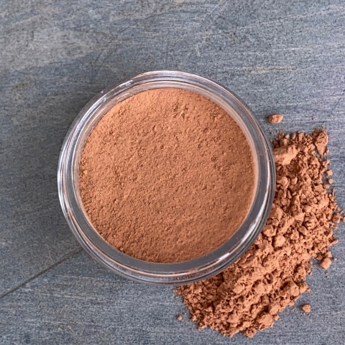 Beach Tan Powder Bronzer: A cosmetic jar with some of the blush powder alongside, showcasing the warm tan hue for a sun-kissed glow