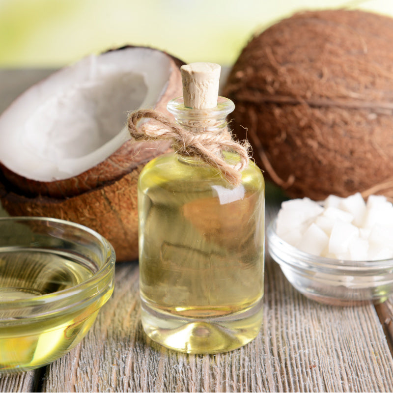 Glass bottle of coconut oil surrounded by coconuts representing product ingredient
