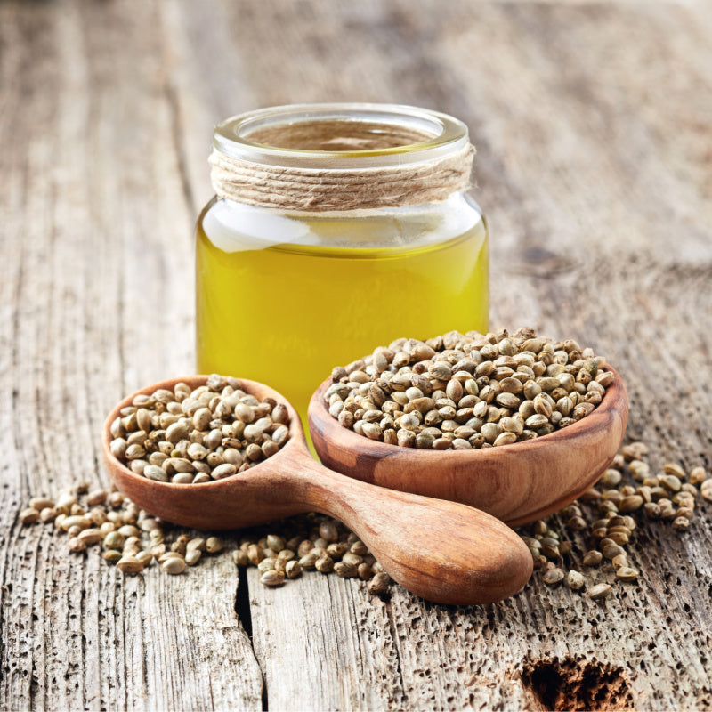 Glass jar of hemp seed oil surrounded by hemp seeds representing product ingredient
