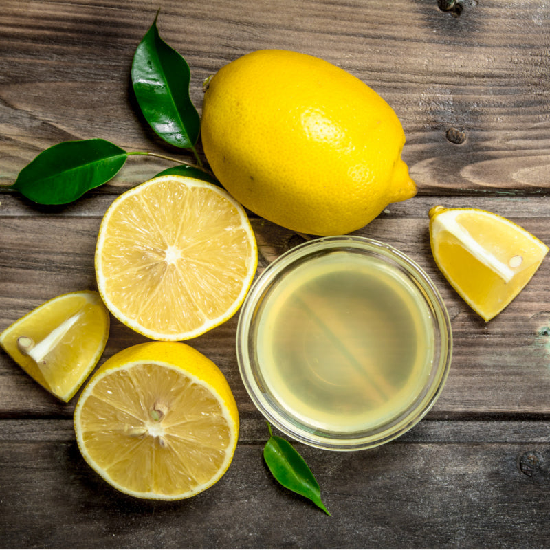 Whole lemons and slices of lemon with juice on wood background with leaves