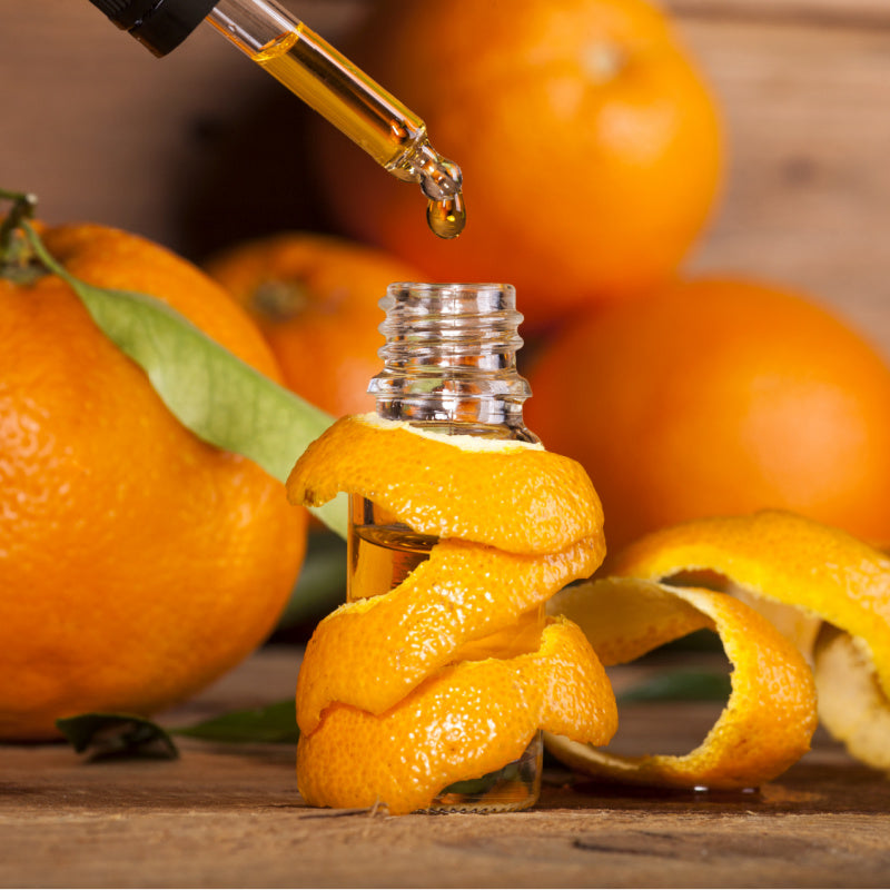 Bottle of orange oil surrounded by orange peels and oranges representing product ingredient 