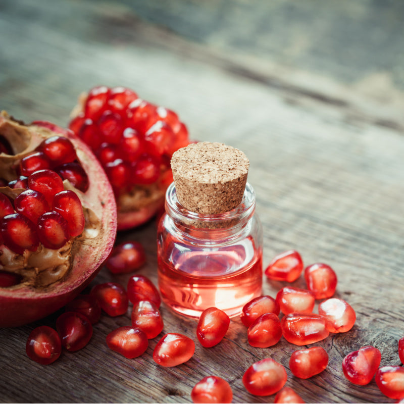 Small glass bottle of pomegranate seed oil surrounded by pomegranate seeds representing product ingredient 